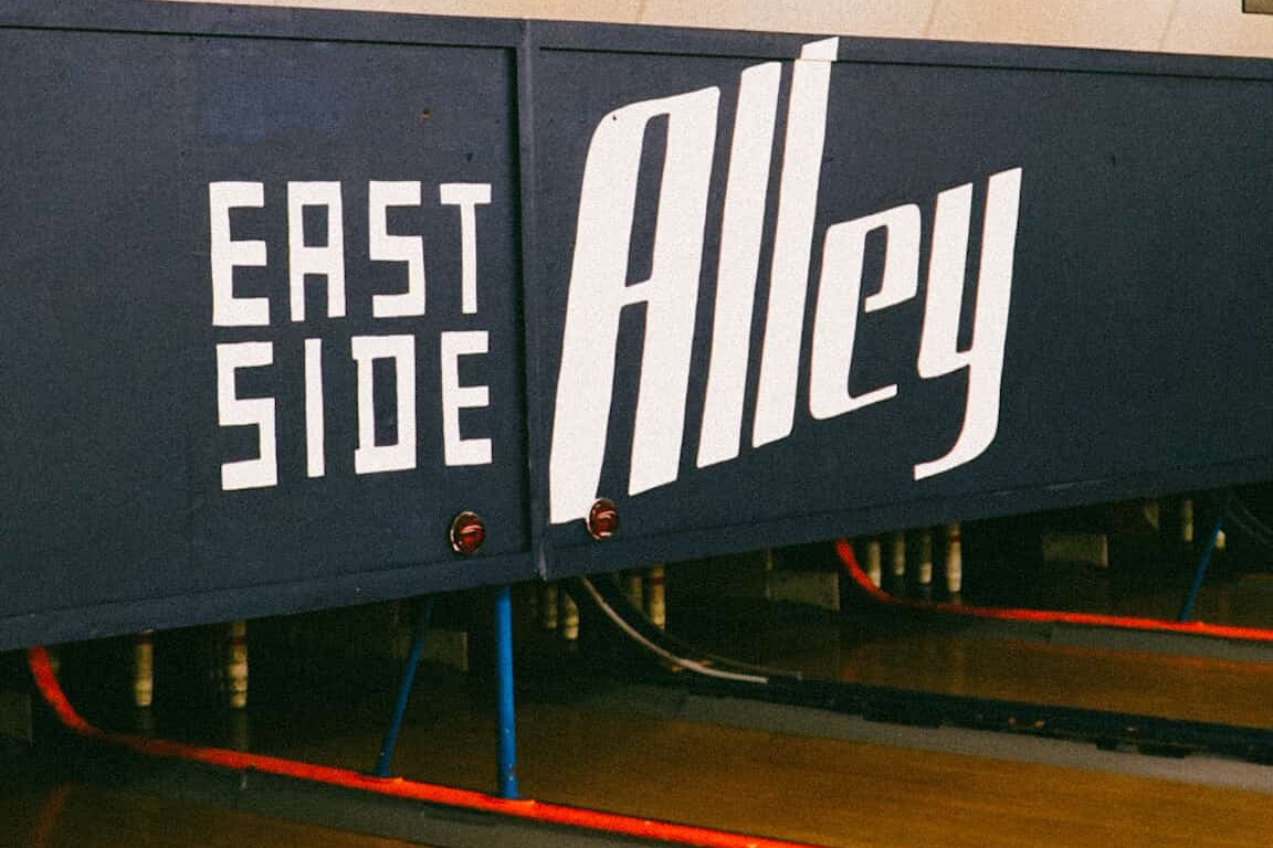 Close-up of a sign with 'East Side Alley' text on a dark background.
