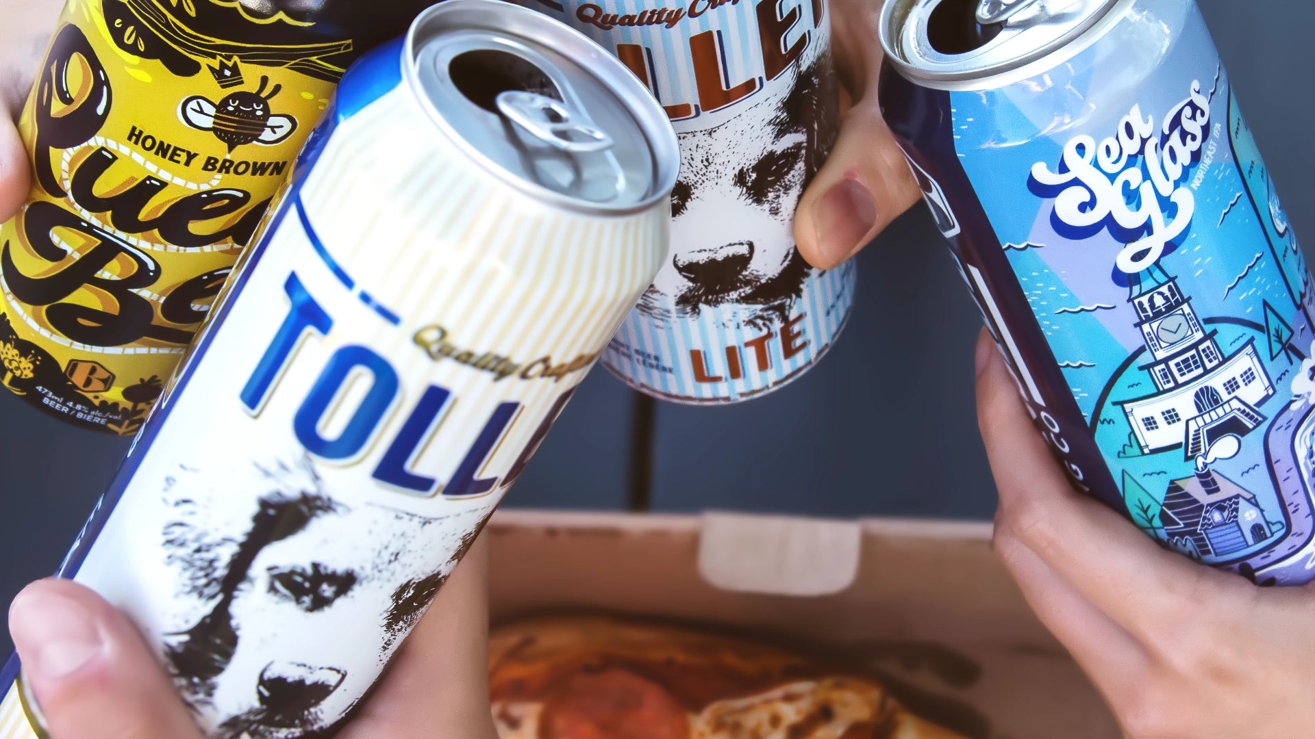 Four craft beer cans held up by hands in front of a pizza box, including Toller Gold, Queen Bee, Toller Lite and Sea Glass.